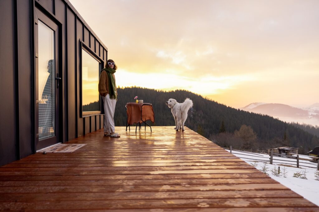 Woman with her dog resting on terrace of tiny house on nature